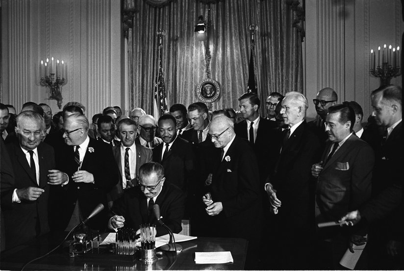 Man signing a document with a crowd around him