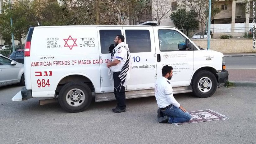 Two men praying in front of a van