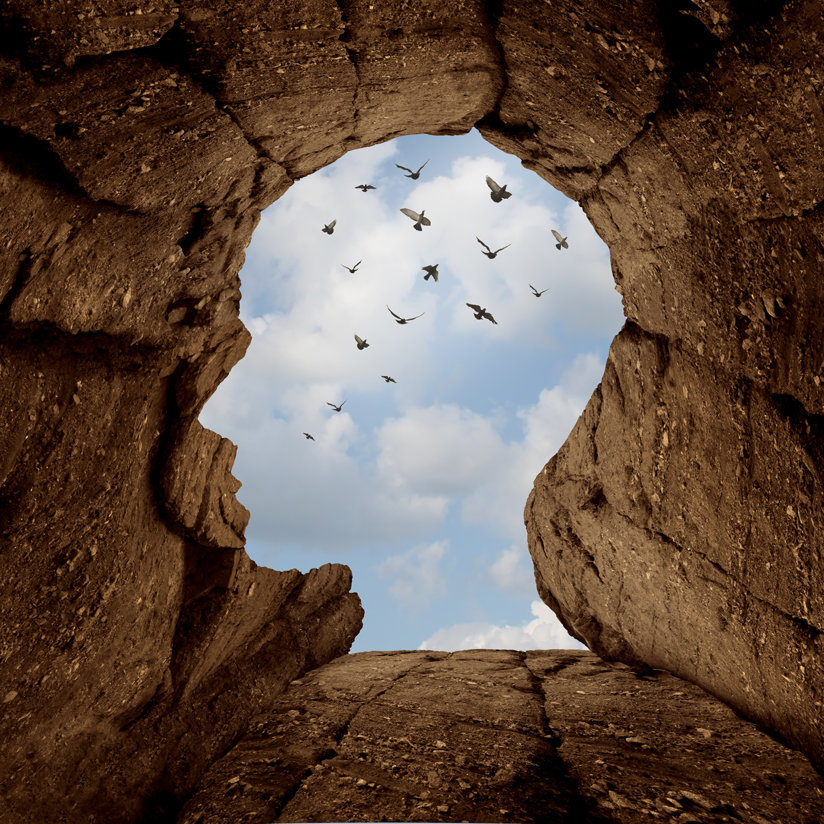 An image of a head carved out in rock with the sky through it