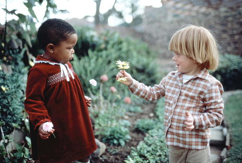 A white boy presenting a black child with a flower